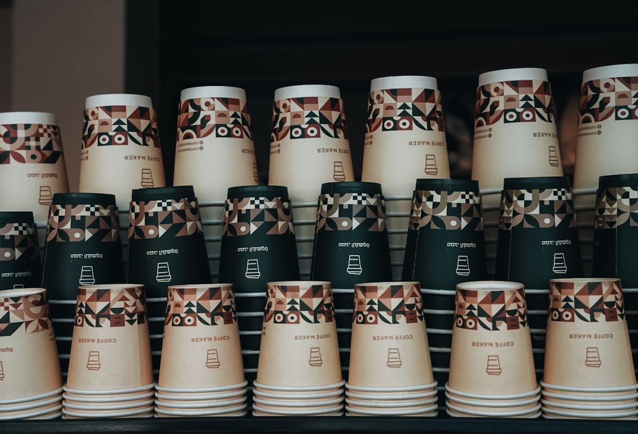 Colorful stack of paper coffee cups with geometric patterns in a cafe setting.